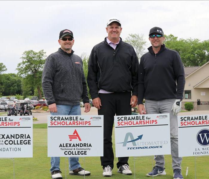 Three men in front of Alexandria Technical College signs at the Scramble for Scholarships at Geneva Golf Course