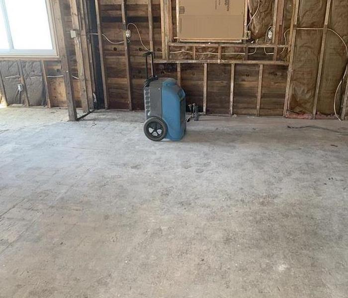 Room with concrete flooring and a blue air mover. 