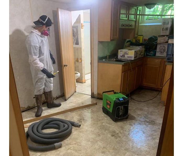 Man in PPE standing in a room with the floors torn up. 